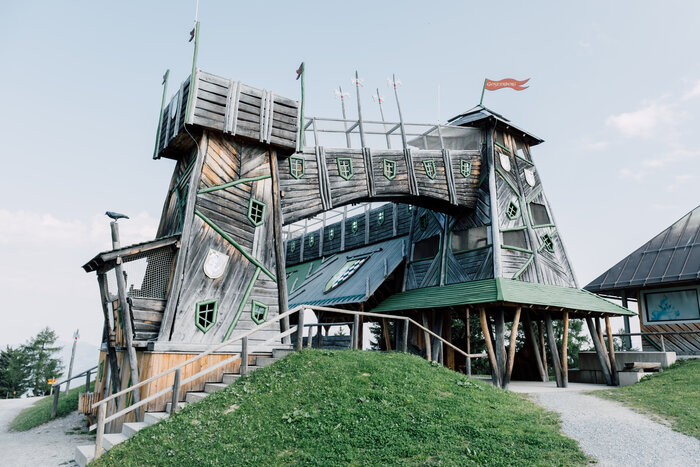 Whimsical wooden castle with towers and a bridge at Geisterberg park, featuring playful green windows and tilted architecture