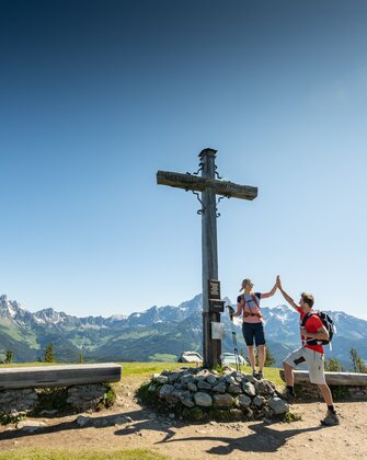 Zwei Personen stehen auf einem Plateau bei einem Gipfelkreuz und geben sich ein High Five | © Tourismusverband Radstadt/Lorenz Masser