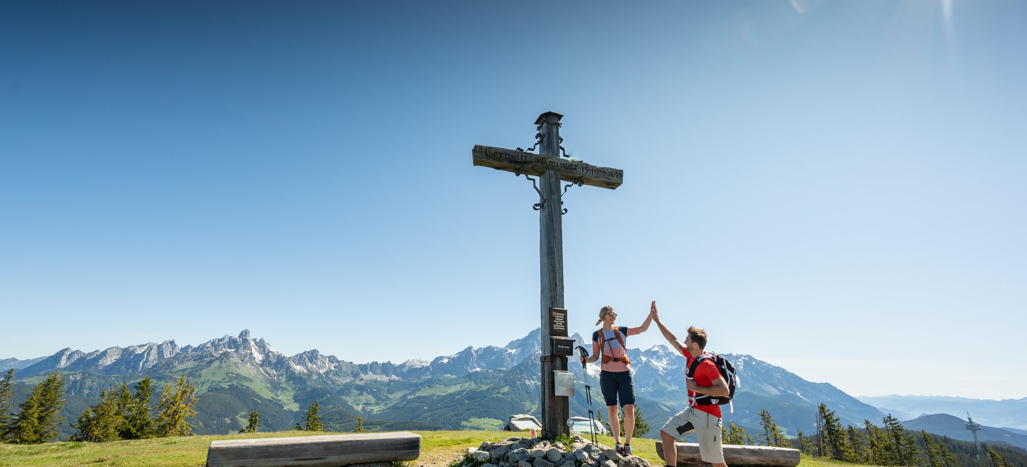 Two people stand on a plateau by a summit cross and give each other a high five | © Tourismusverband Radstadt/Lorenz Masser