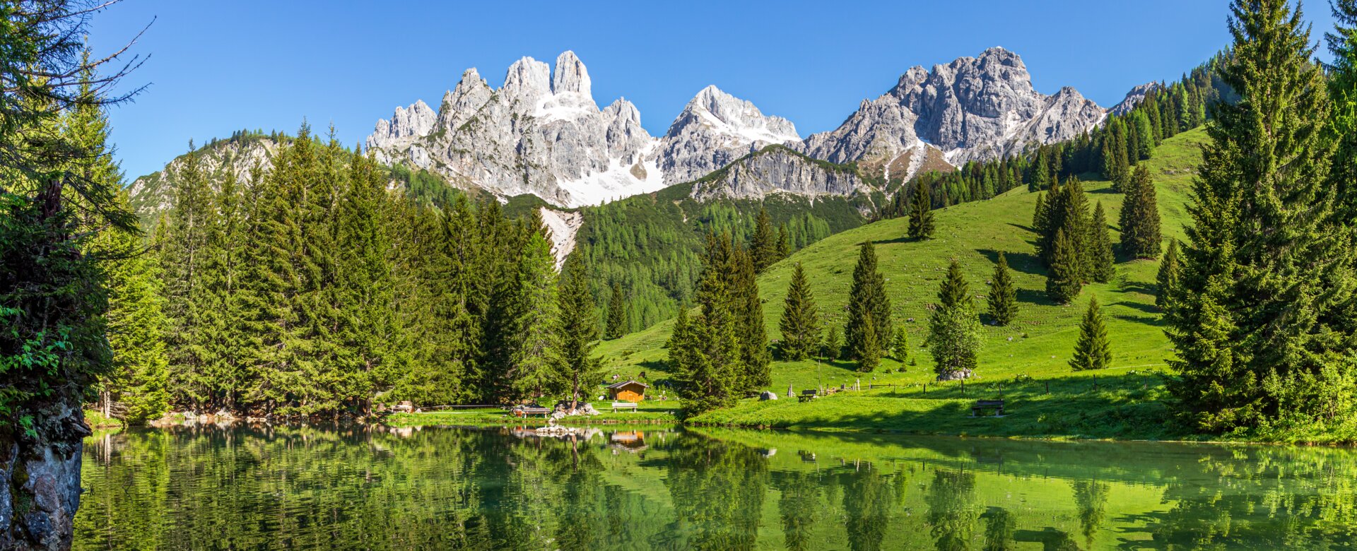 Crystal-clear Almsee reflecting the Bischofsmütze mountain, green meadow and forest in summer near Filzmoos, Austria | © CoenWeesjes