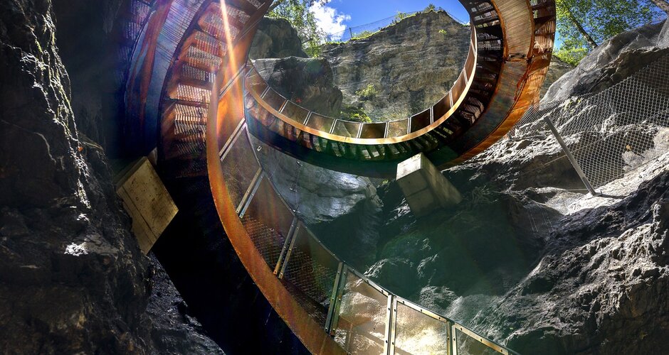 Spiral metal walkway in Liechtenstein Gorge between rock walls under blue sky with bright sun. | © Walter Oczlon