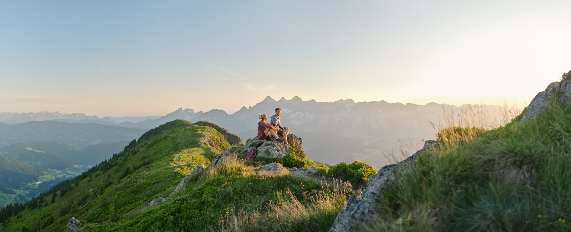 Two hikers sit on a rock and enjoy the mountain view during sunrise on the Reiteralm | © Peter Burgstaller