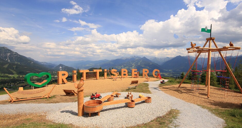 Panoramic playground with wooden letters, swings and water play set against mountains on Rittisberg | © Photo Austria, Hans-Peter Steiner