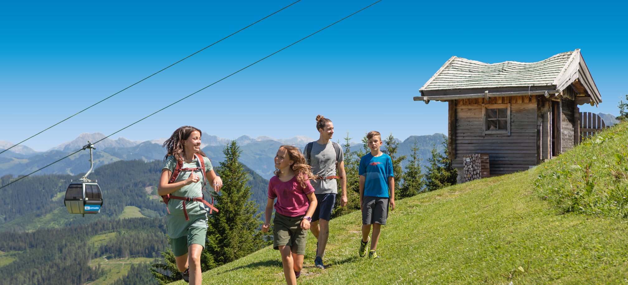 Group of four hikers enjoys a sunny day on the alpine meadow with gondola view and wooden hut in the background in Ski amadé.