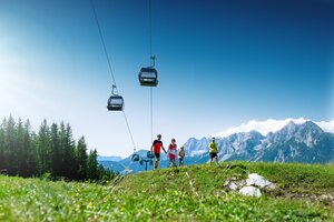 Family hiking on alpine meadow with gondola and mountain backdrop