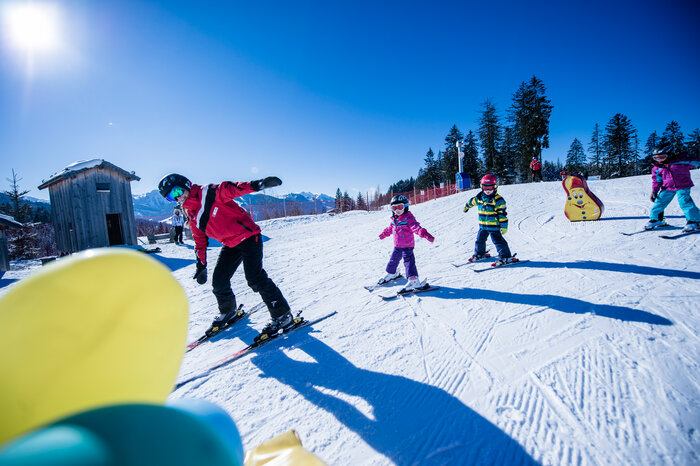 Children in colorful ski class with instructor on a sunny slope, learning to ski together on the snowy slope.