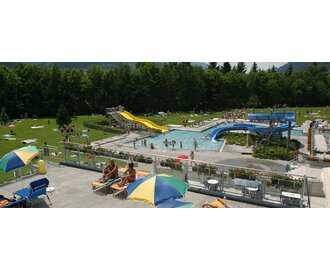 Summery pool with slides, a swimming area, and a green sunbathing lawn surrounded by nature.