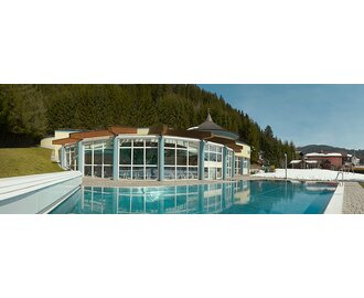 Thermal spa with an outdoor pool, surrounded by mountains and forests in the winter landscape.