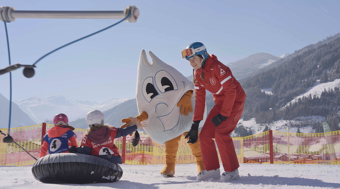 Two kids sit on snow tubes in Dorfgastein snow park, mascot Gasti and instructor greet them with smiles | © Dorfgasteiner Bergbahnen