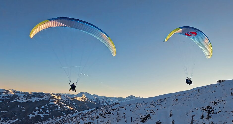 Two people glide in tandem paragliders above snowy mountain landscape at sunset in Dorfgastein | © Dorfgasteiner Bergbahnen
