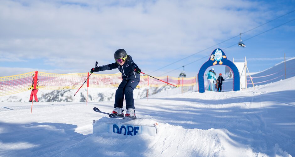 Child in ski gear jumps over ramp in practice area with archway and safety netting in Dorfgastein | © Dorfgasteiner Bergbahnen