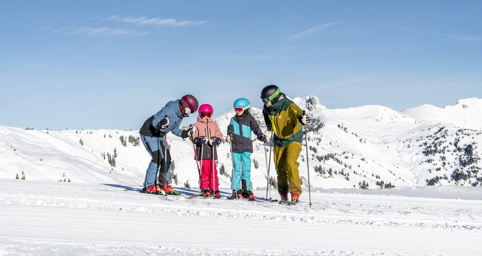 Four-member skiing family standing together on wide slope in Dorfgastein with snowy mountain landscape behind | © Dorfgasteiner Bergbahnen
