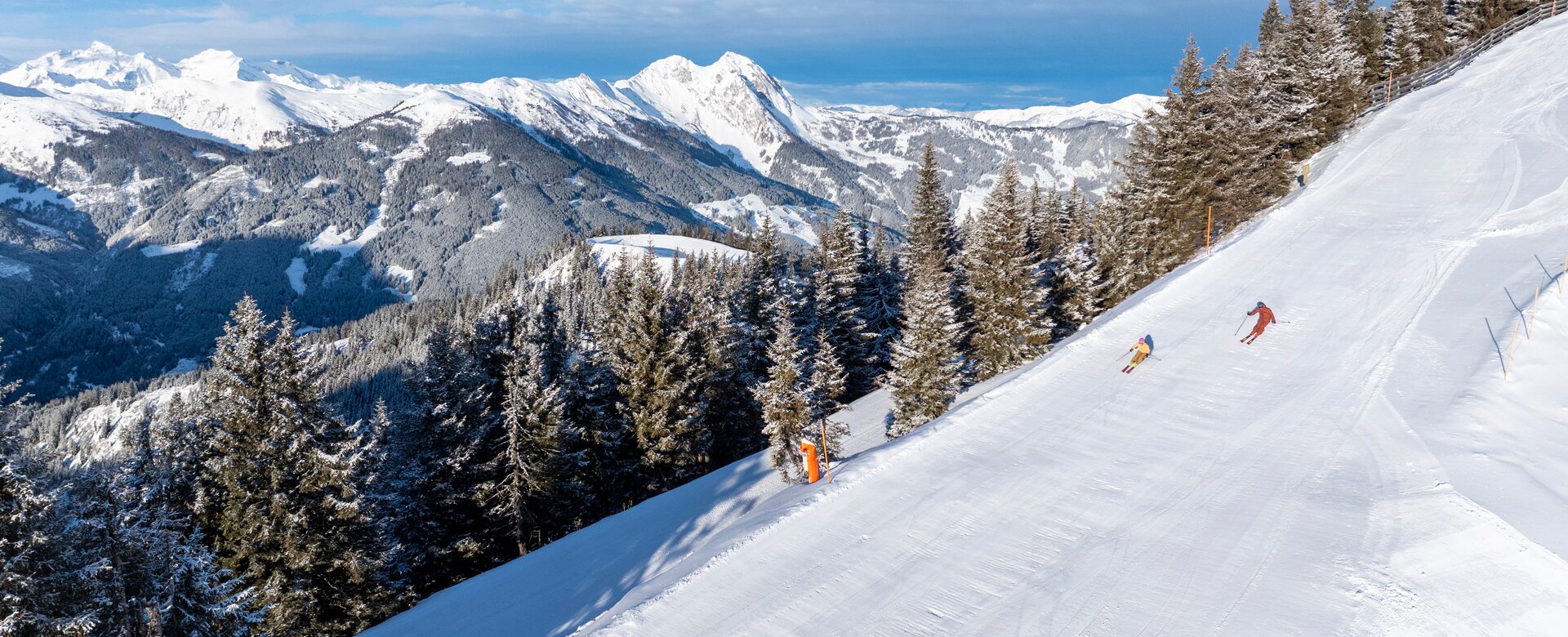 Two skiers descend on groomed panoramic slope in Dorfgastein, surrounded by snowy trees and alpine mountain view | © Dorfgasteiner Bergbahnen