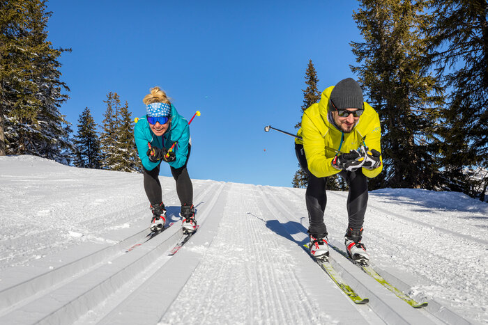 Two cross-country skiers crouching along the trail