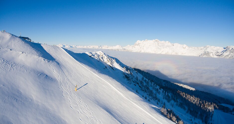 Snowy summit with skiers, blue sky, and view into the snowy valley.