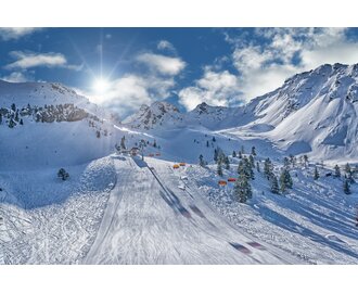 Ski slope with orange chairlifts, sun, and snowy mountains at Hauser Kaibling.