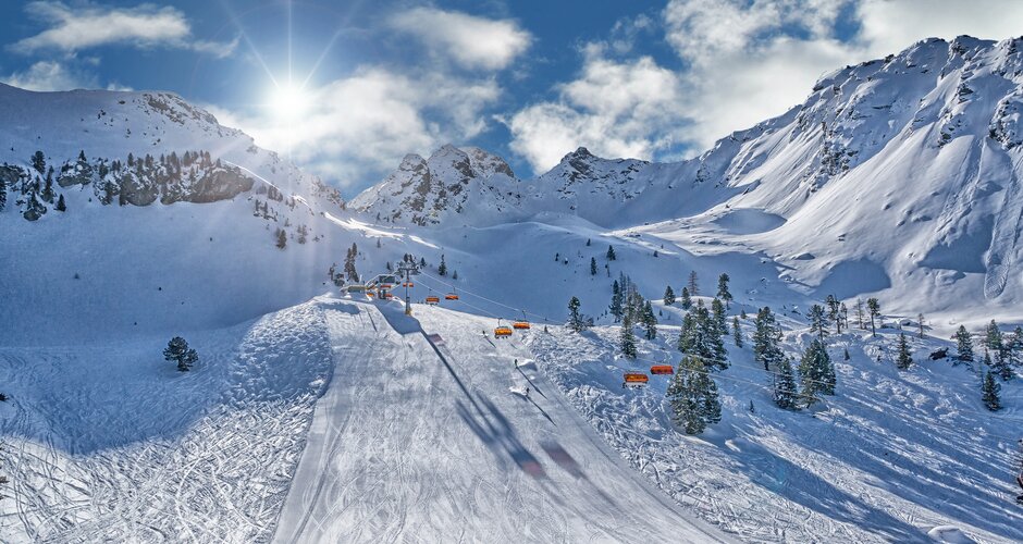Ski slope with orange chairlifts, sun, and snowy mountains at Hauser Kaibling.