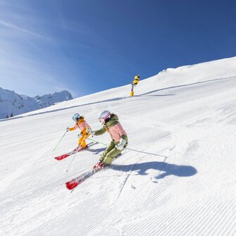 Two skiers descend a freshly groomed slope under bright sunshine. | © Bernhard Moser