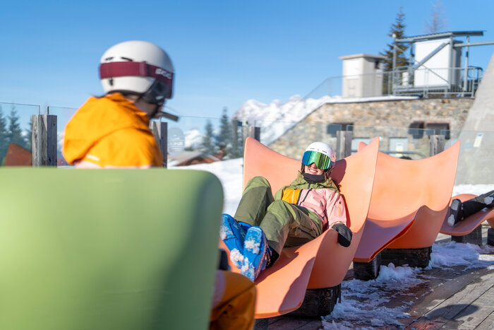 Two skiers relaxing in orange loungers at the Genussinsel in the snow. | © Bernhard Moser