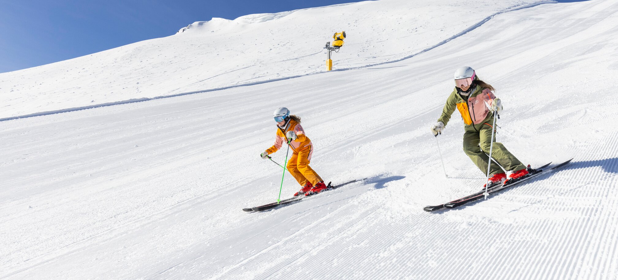 Two skiers carve turns on freshly groomed slopes at Hauser Kaibling, surrounded by snowy hills under a clear blue sky. | © Bernhard Moser