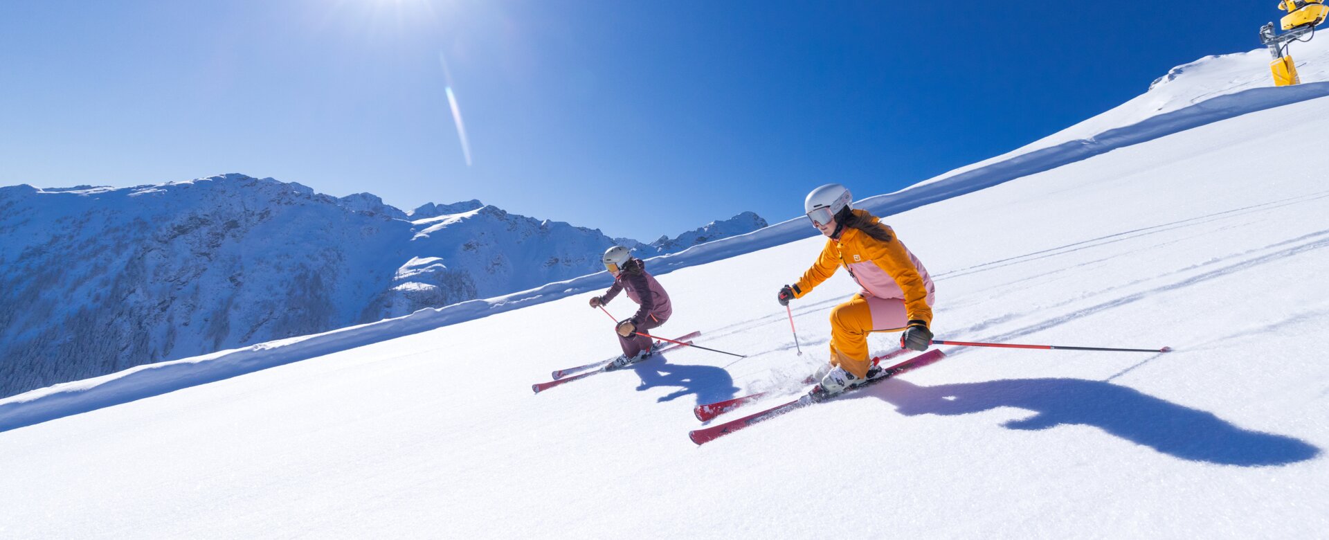 Two skiers ride in the sun on a groomed slope covered with fresh snow. | © Hauser Kaibling