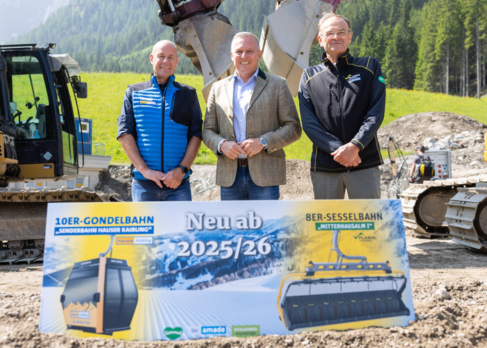Three men stand by excavators and a sign for new lifts starting in the 2025/26 season. | © Harald Steiner
