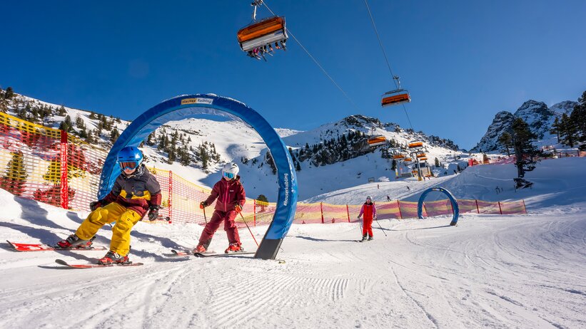 Kids skiing through blue gates on the XXL funslope at Hauser Kaibling in bright sunshine. | © Hauser Kaibling