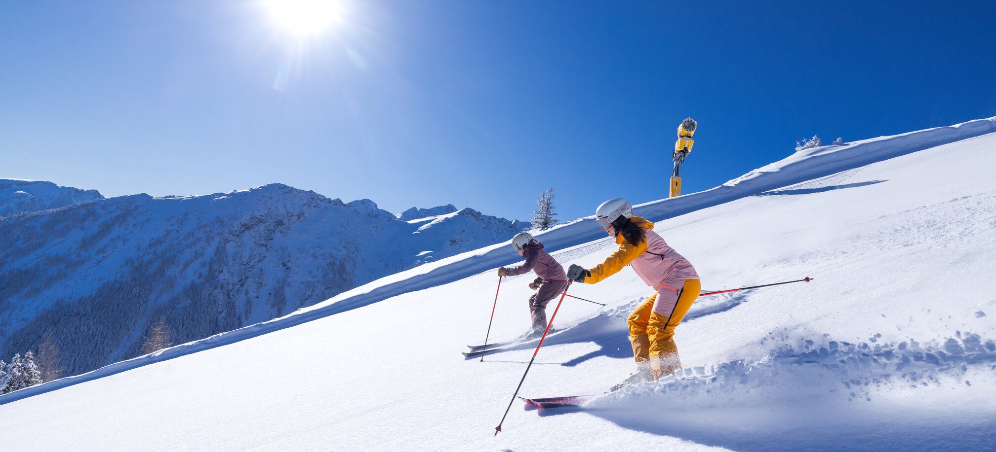 Two skiers ride in the sun on a groomed slope covered with fresh snow. | © Hauser Kaibling