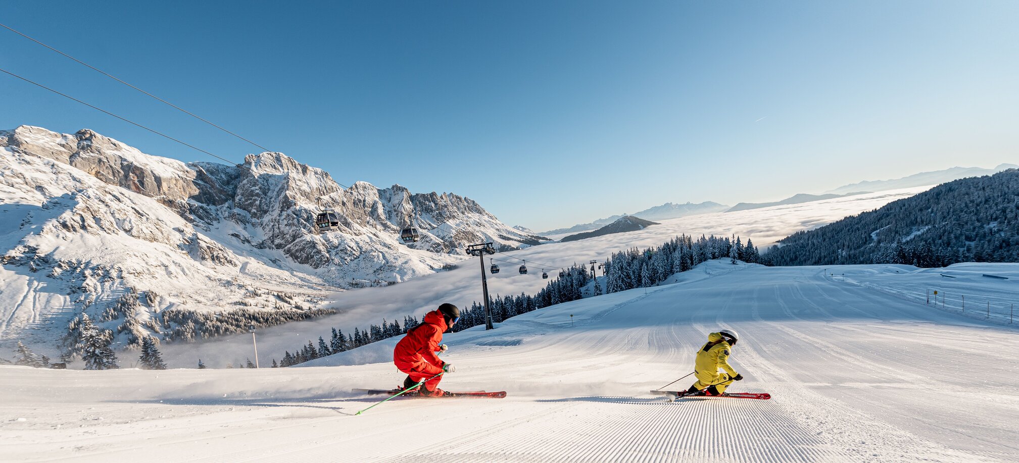 Two skiers at sunrise on freshly groomed slope in Mühlbach with alpine backdrop | © Hochkönig Tourismus GmbH