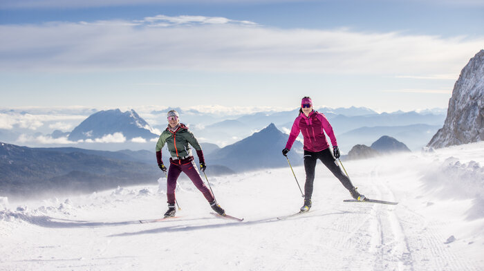 Two cross-country skiers in winter landscape at Dachstein, snow and mountains in the background. | © Harald Steiner