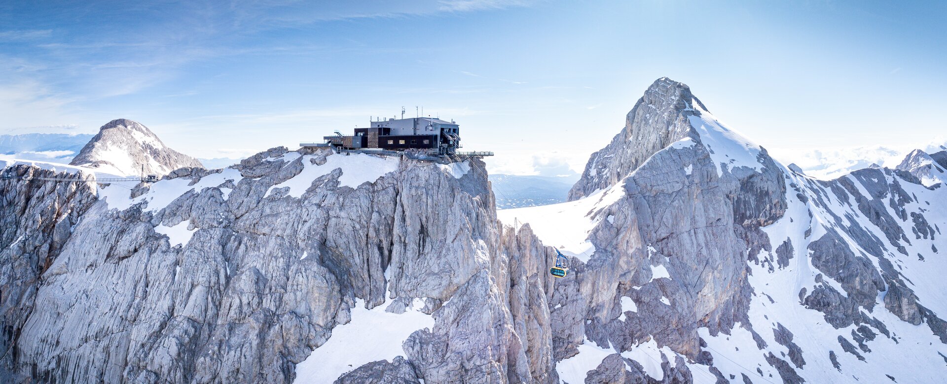 Dachstein glacier cable car rides between snow-covered peaks under a blue sky. | © Josh Absenger