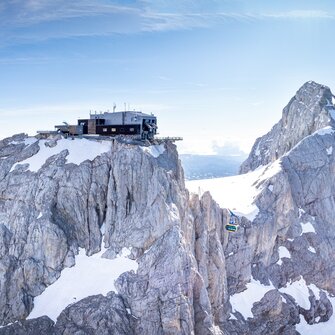 Dachstein glacier cable car rides between snow-covered peaks under a blue sky. | © Josh Absenger