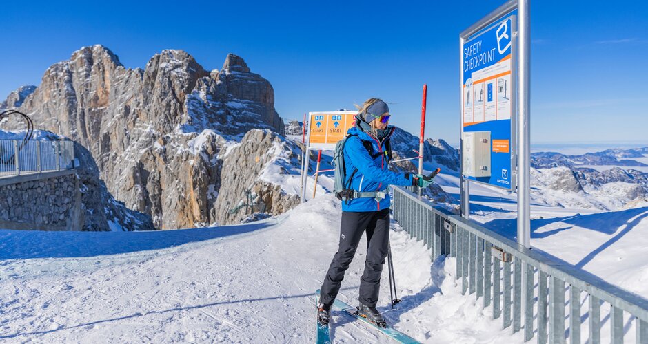 Skier checks avalanche transceiver at safety checkpoint with rocky mountain backdrop. | © René Eduard Perhab