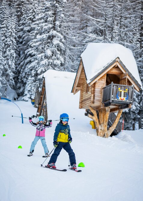 Two kids skiing in front of snow-covered trees and a hut at Galstiland Galsterberg. | © Mirja Geh