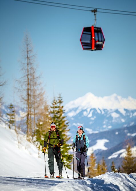 Two ski tourers climb up a groomed ski tour route in sunny weather. | © Christoph Huber