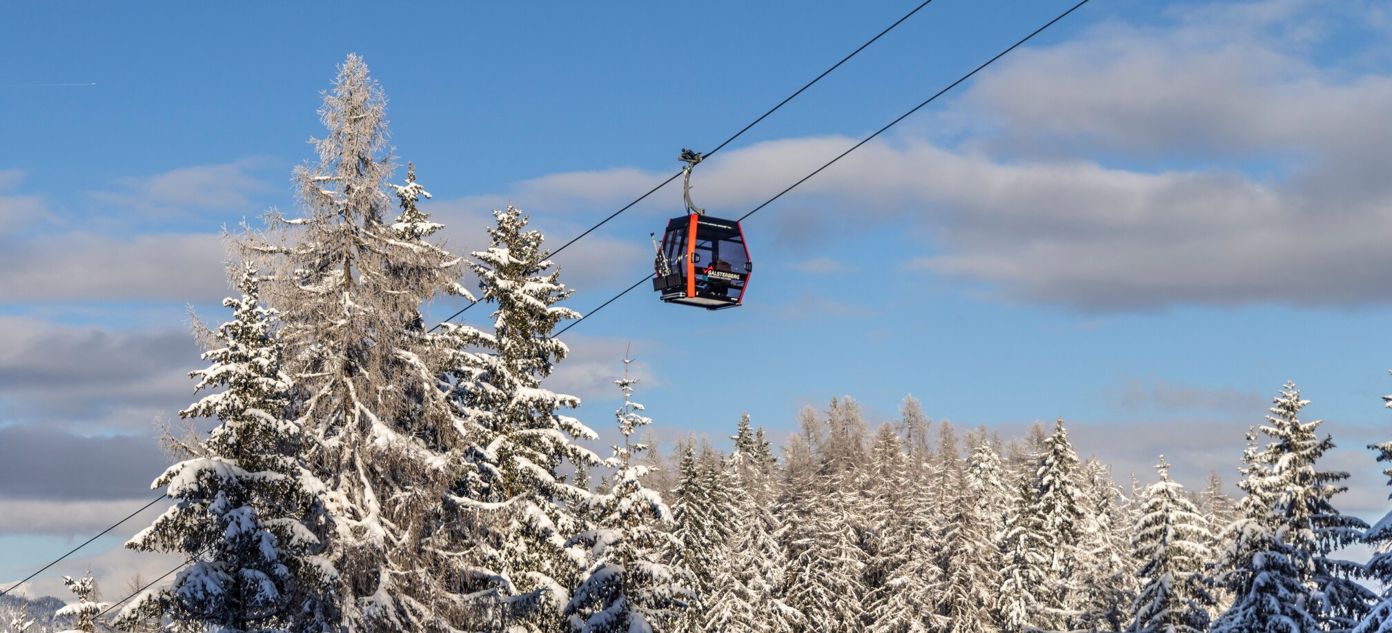 Red gondola traveling through a snowy winter forest at Galsterberg in sunshine. | © Mirja Geh