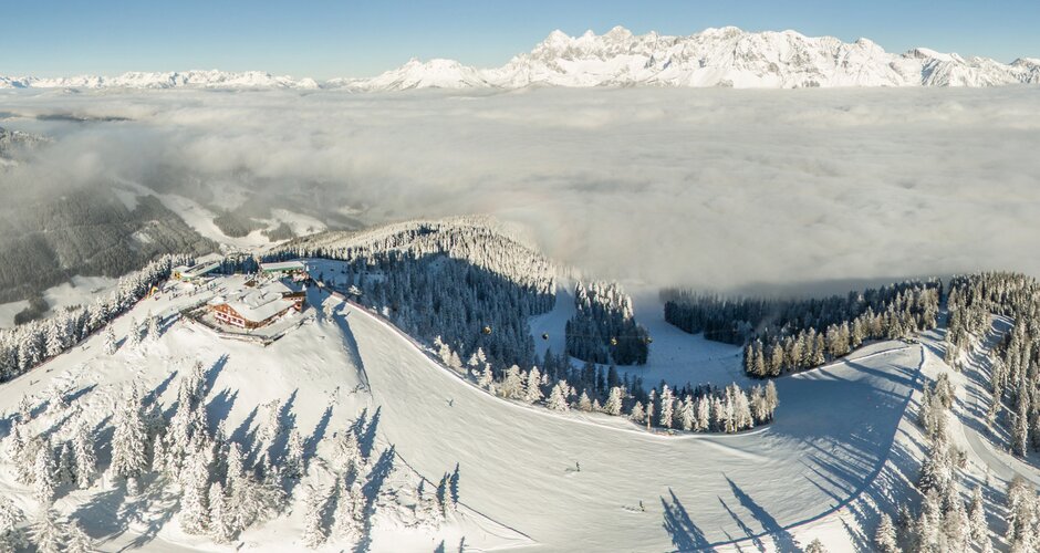 Aerial view of snow-covered ski slopes on Hochwurzen with a sea of clouds in the background. | © Bence Bankuty