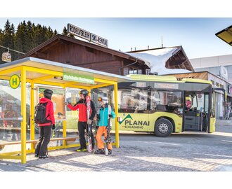 Skiers with equipment at Hochwurzen ski bus stop, ski bus in background. | © David Stocker