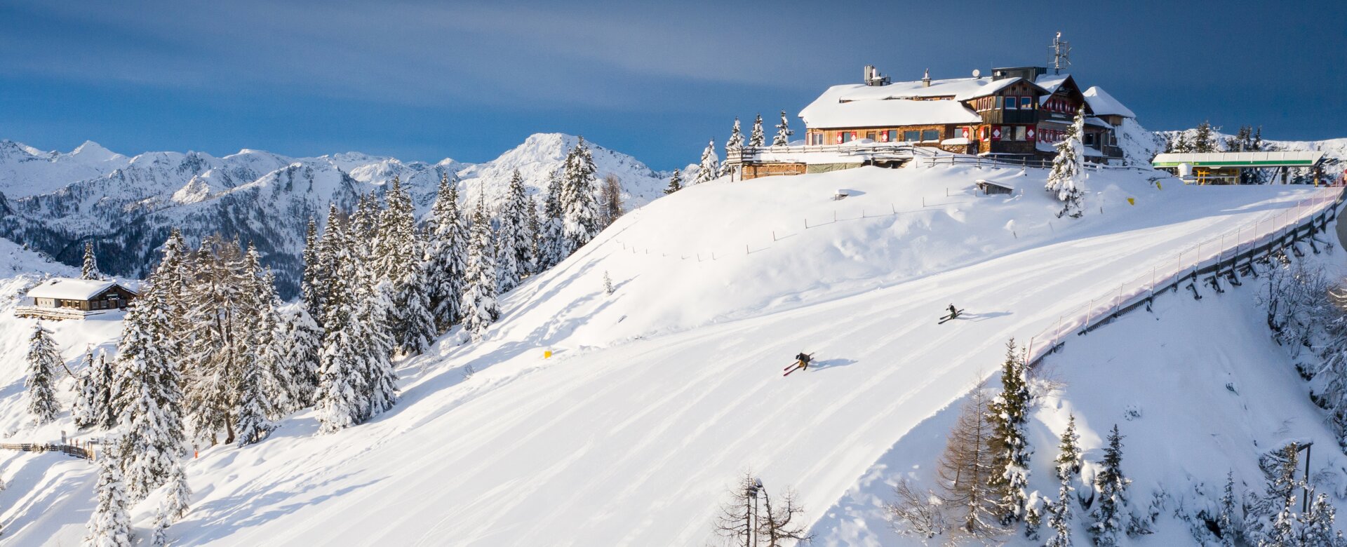 Skiers and snowboarders on a snowy slope with a mountain panorama. | © Josh Absenger