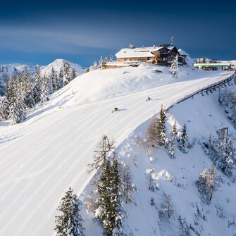 Skiers and snowboarders on a snowy slope with a mountain panorama. | © Josh Absenger