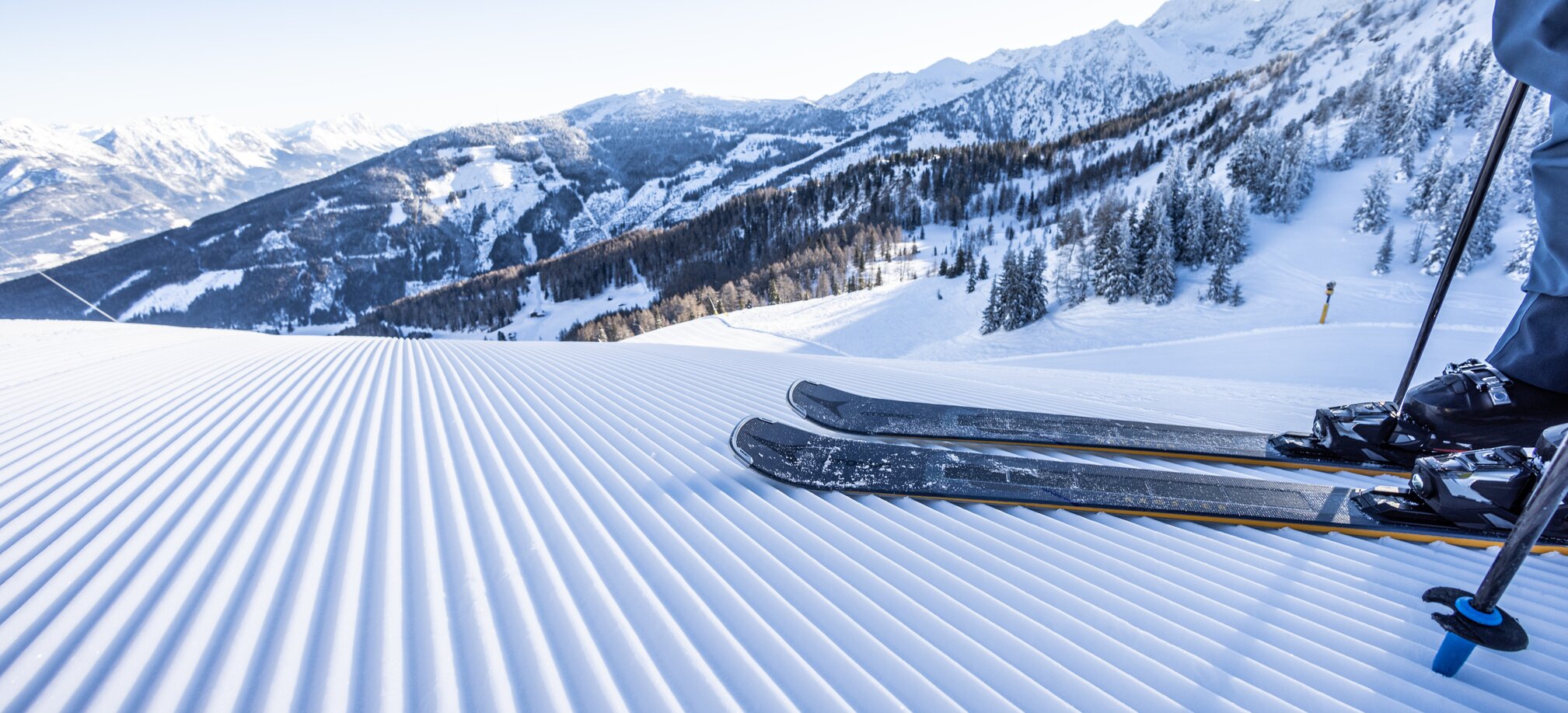 Skis on a freshly groomed slope with a snowy alpine landscape in the background. | © Mirja Geh