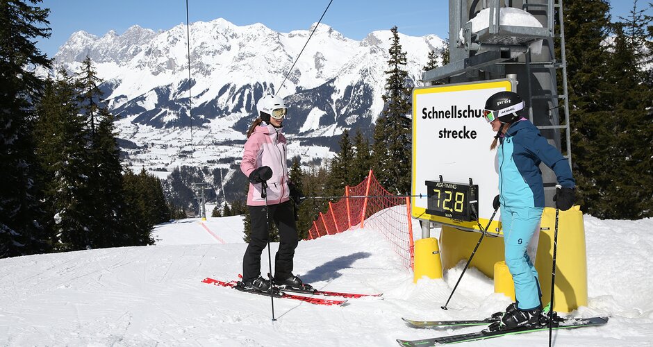 Two female skiers at the speed check course on Planai, one looking at the digital speed display showing 72.8 km/h. | © Herbert Raffalt