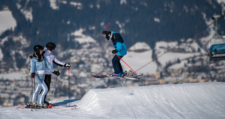 Skier in blue gear jumps at Beginnerpark with snowy backdrop.