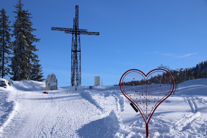 Prepared snow path leads to metal cross and a red metal heart stands in the foreground