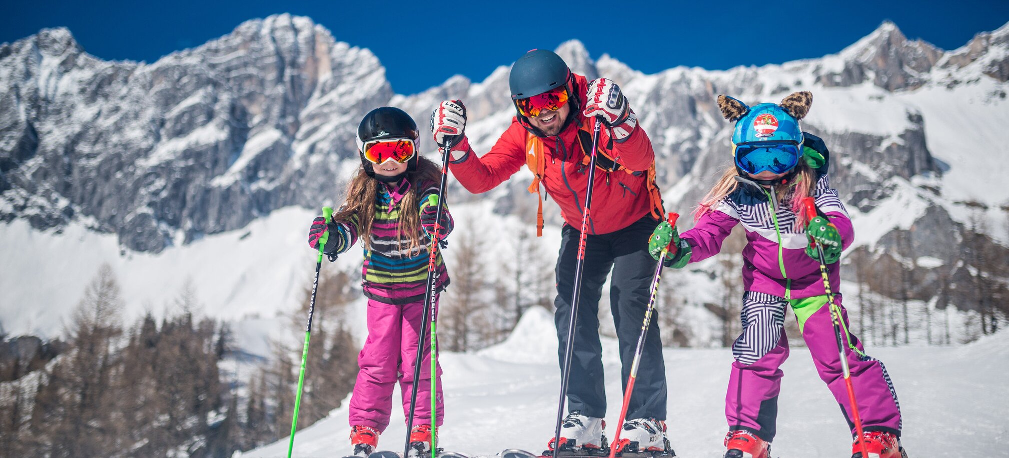 Family with two children skiing in front of a snow-covered mountain backdrop. | © Christine Höflehner