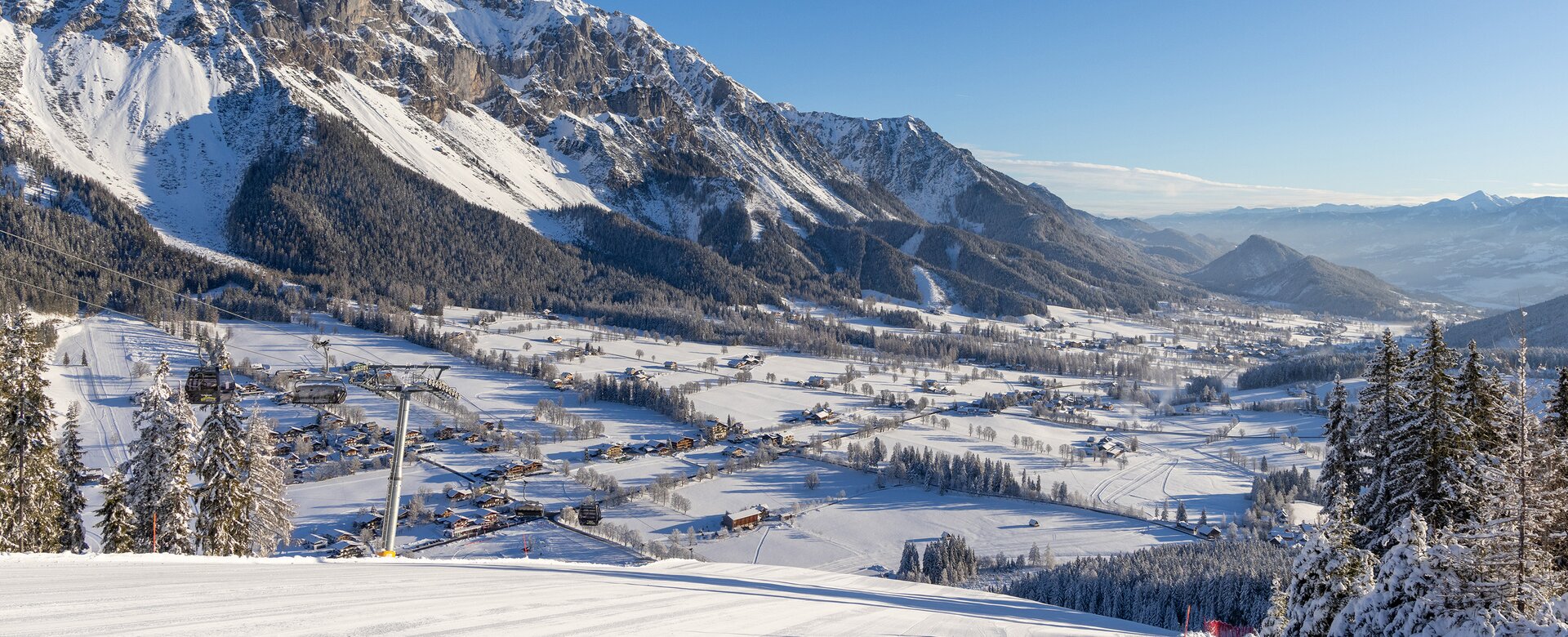 View from groomed ski slope of snowy Enns Valley and striking mountain backdrop.