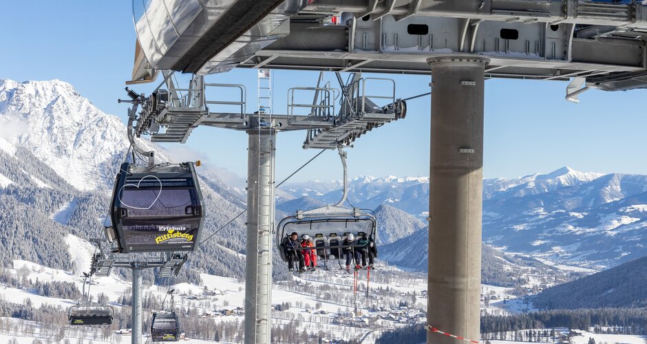 Menschen fahren im Sessellift und Gondeln über verschneite Landschaft am Rittisberg.