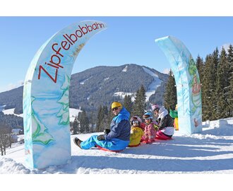 Four kids and two adults on Zipfelbobs under the arch of the Zipfelbob track | © Hans-Peter Steiner