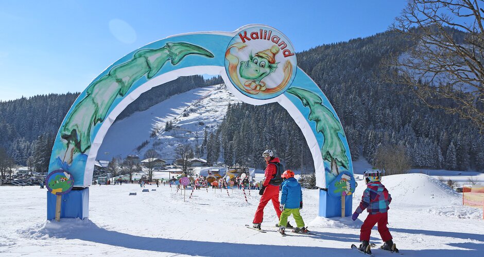 Three children skiing under colourful Kaliland archway in Ramsau