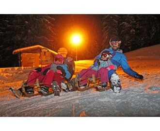 Two adults and two kids tobogganing at night on Rittisberg under floodlight